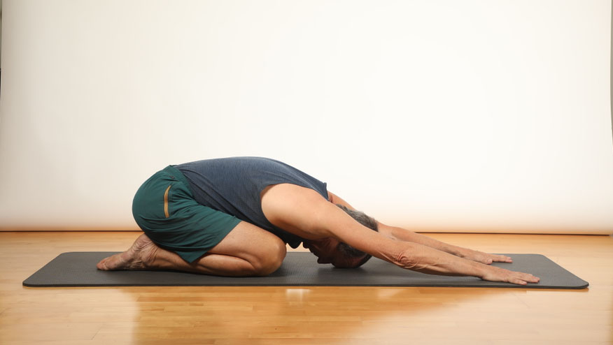 A person in the Child’s Pose yoga position, kneeling with arms extended forward on a yoga mat, forehead resting on the floor